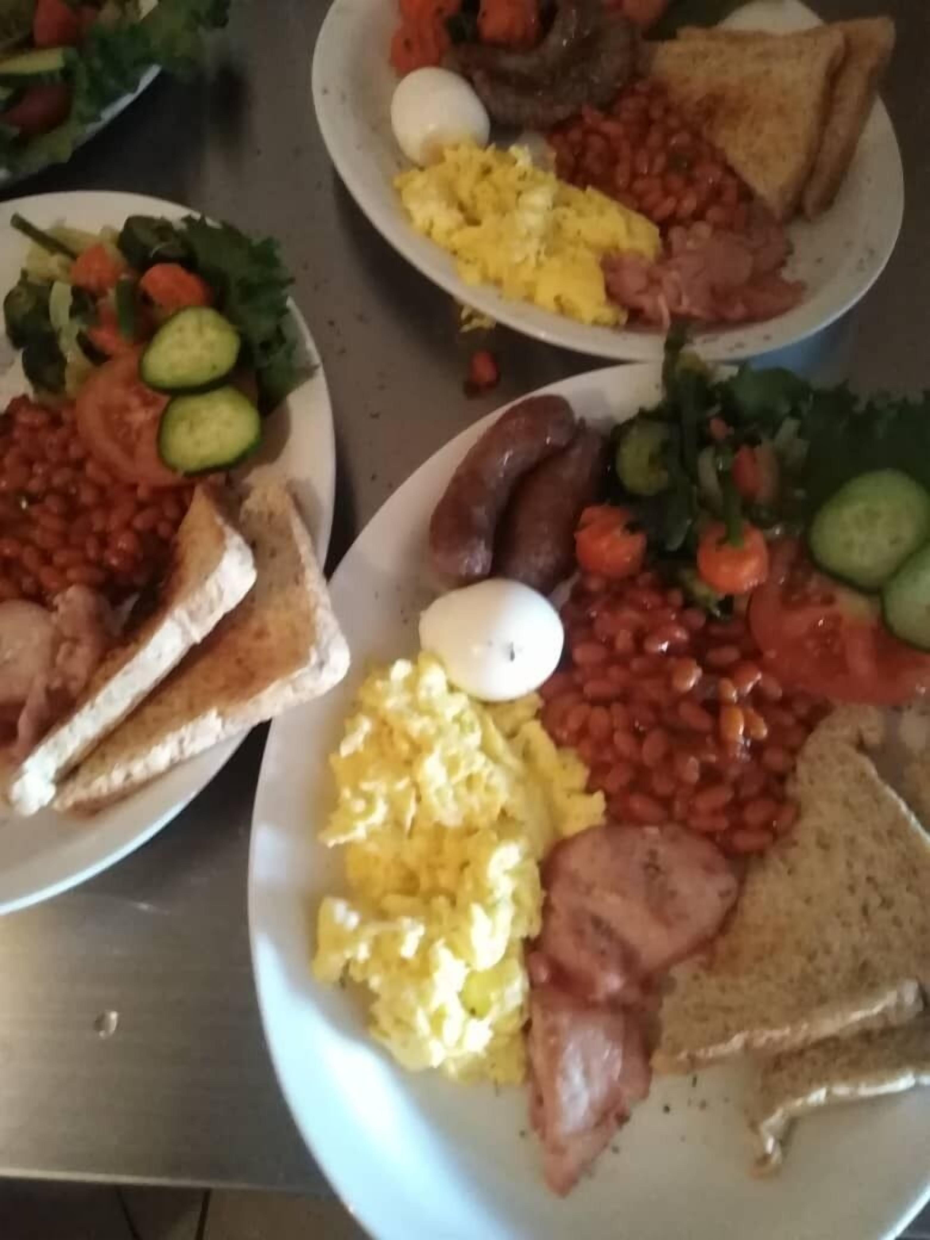 A table with three plates of breakfast food including toast, eggs, beans, sausages, and vegetables.