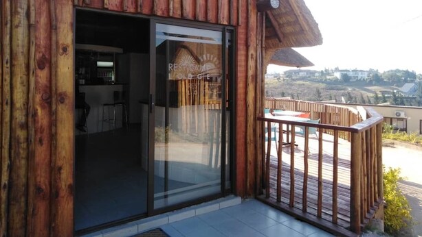 Un edificio de madera con puerta de vidrio que da a un espacio interior, un balcón con barandilla y vistas a un paisaje montañoso.