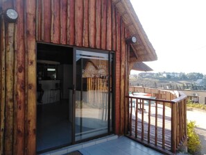 A wooden building with a glass door leading to an interior space, a balcony with a railing, and a view of a hilly landscape. - Rest Camp Lodge (Manzini)
