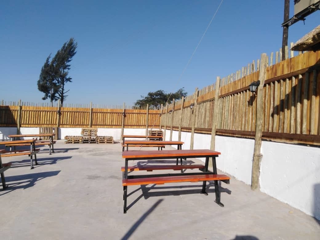 Un patio al aire libre con bancos y mesas de madera, rodeado por una valla de madera y una pared blanca.