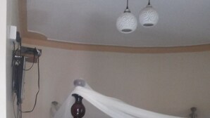 Ett sovrum med en säng med himmelstänger i trä, ett sänghimmel, ett rosa överkast med ett Hello Kitty-mönster och ett sängbord med en lampa.