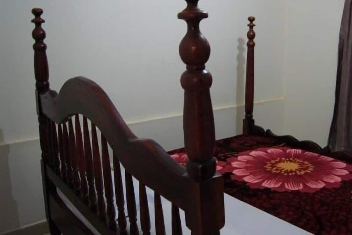 A bedroom with a wooden four-poster bed, a red floral bedspread, and a white pillow.