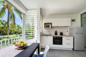 A modern kitchen with white cabinets, a microwave, and a refrigerator. There is a dining table with a bowl of fruit and a chair.