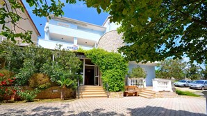 L'ingresso di un hotel con vialetto lastricato, una scalinata che conduce all'ingresso e un grande albero sullo sfondo.