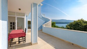 Un balcone con tavolo e sedie rossi, una porta vetrata e vista sul mare e sulle montagne.