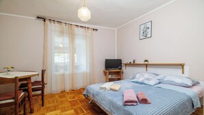 Ein Schlafzimmer mit Bett, Schreibtisch, Stuhl, Fernseher und einem Fenster mit Vorhängen.
