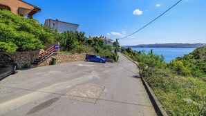 Eine Küstenstraße mit einem blauen Auto, das am Straßenrand geparkt ist, einer Steintreppe und Blick auf das Meer.