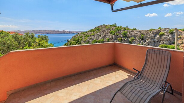 Ein Balkon mit Blick auf das Meer und die Hügel, ein gestreifter Stuhl und ein rotes Dach.