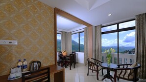 A hotel room with a dining area, a view of mountains, and a balcony with a table and chairs. - Tea Castle Munnar (Devikolam)