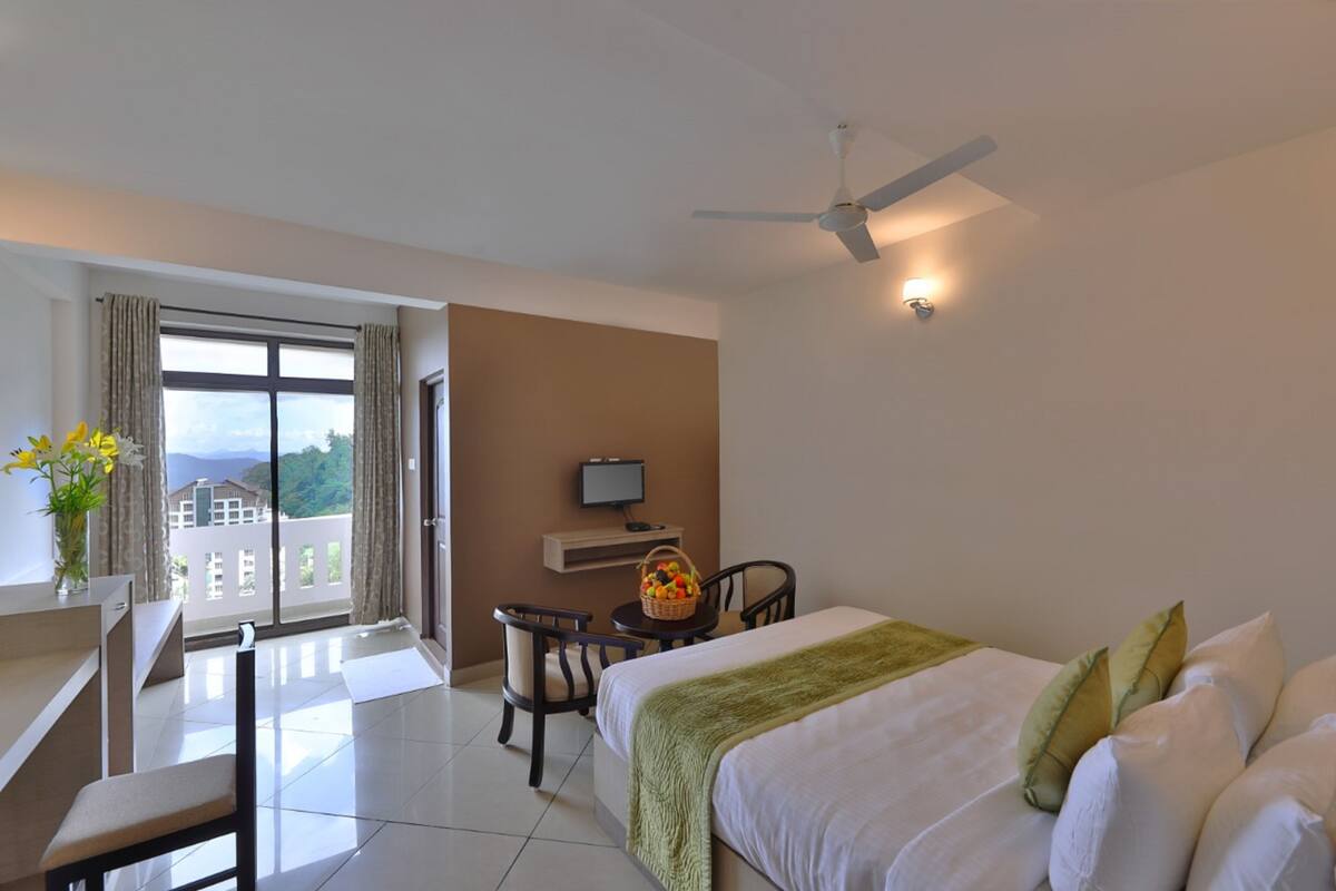 A hotel room with a bed, a desk with a chair, a television, and a balcony with curtains.