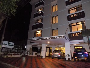 A multi-story hotel with a covered entrance and a parking area. - Tea Castle Munnar (Devikolam)
