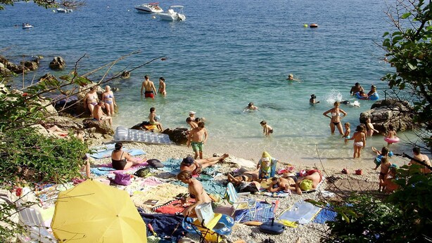 A crowded beach with people swimming and sunbathing, boats in the water, and umbrellas on the sand. - Apartment Marija (Novi Vinodolski)