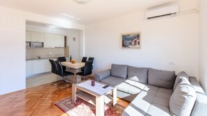 A modern living room with a grey sofa, a dining table with chairs, and a kitchen area in the background. - Apartment Marija (Novi Vinodolski)