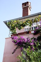 Un edificio con fachada rosa, una chimenea de ladrillo y plantas en macetas en el balcón.