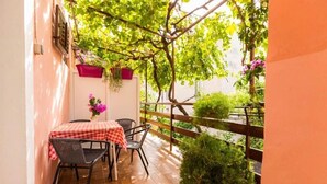 A small outdoor patio with a table and chairs, surrounded by greenery and a wooden fence. - Apartments Vodaric (Mali Losinj)
