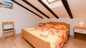 A bedroom with a sloped ceiling, a bed with a quilt, a chair, a bedside table with a lamp, and a small cabinet. - Apartment Mauro (Punat)
