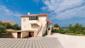 A two-story building with a red-tiled roof, a staircase leading to the upper floor, and a view of the sea in the background. - Apartment Mauro (Punat)