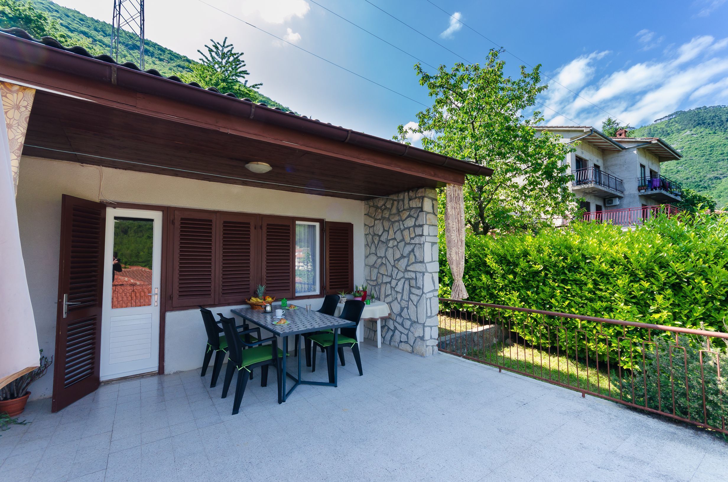 A patio with a table and chairs, a stone wall, and a view of a hillside.