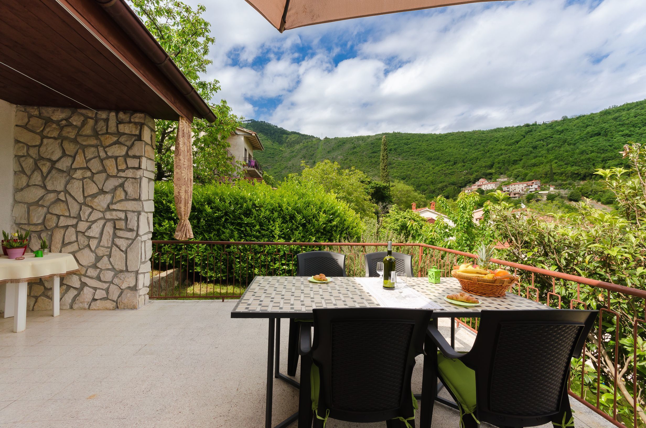 Une terrasse extérieure avec une table dressée pour deux personnes, entourée de murs en pierre et offrant une vue sur une colline verdoyante.