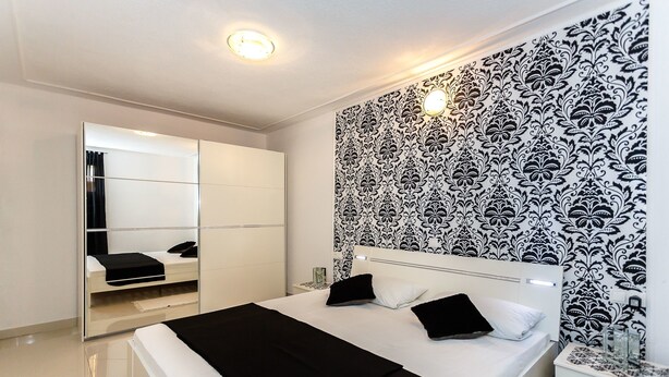 A modern bedroom with a large bed, a wardrobe, and a patterned wallpaper. - Apartments and Rooms Gordana (Malinska)