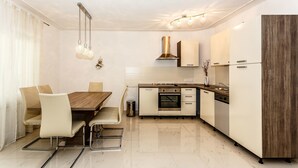 A modern kitchen with a dining area, featuring a wooden table, white chairs, a built-in oven, and a stainless steel range hood. - Apartments and Rooms Gordana (Malinska)