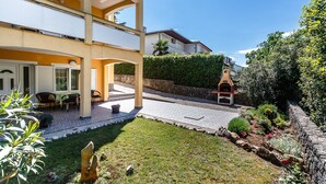 A two-story residential building with a patio area, outdoor seating, and a small garden. - Apartments and Rooms Gordana (Malinska)