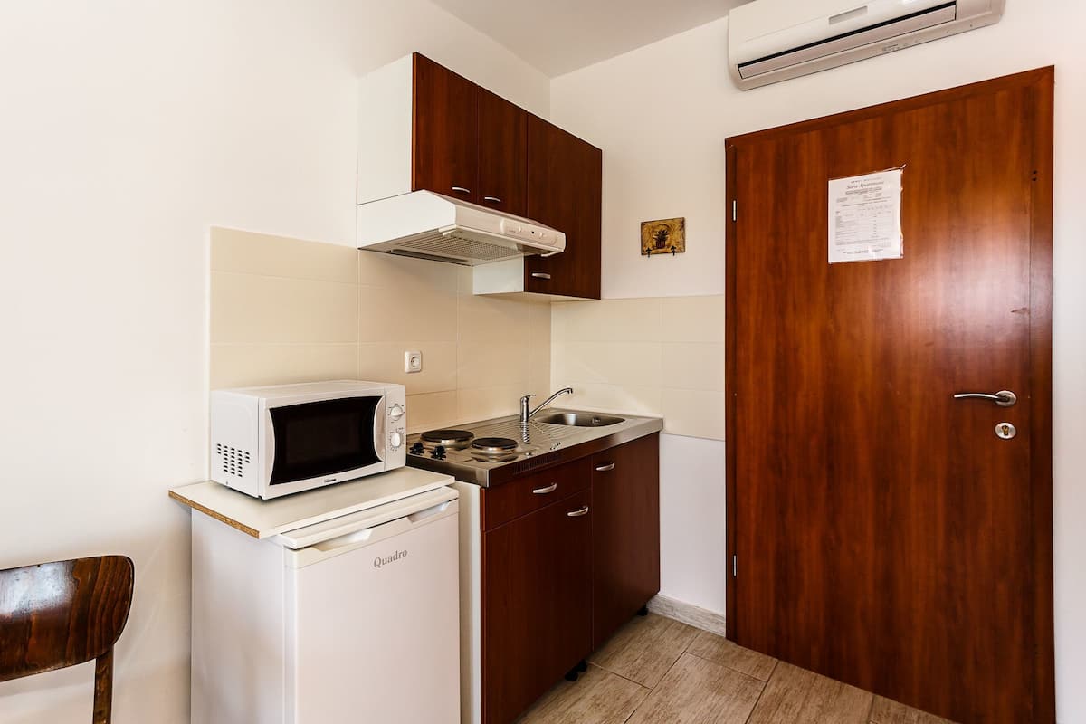 A compact kitchen with a white microwave, a small refrigerator, wooden cabinets, a sink, and a door with a notice.