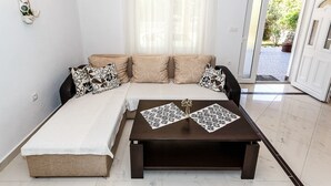 A living room with a sofa, two patterned throw pillows, a coffee table with decorative items, and a view of the outside through a door. - Apartments and Rooms Gordana (Malinska)