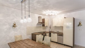 A modern kitchen with a wooden dining table and chairs, a built-in oven, and a refrigerator. - Apartments and Rooms Gordana (Malinska)
