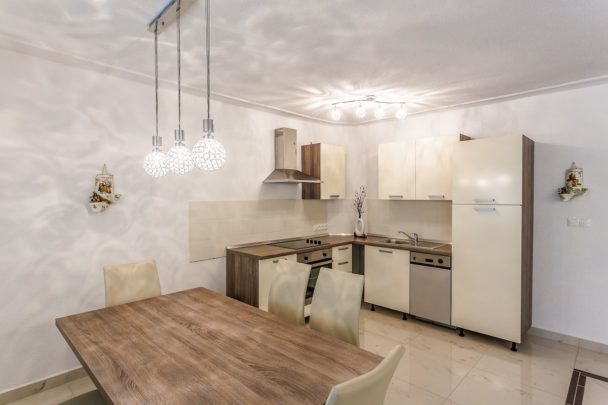 A modern kitchen with a wooden dining table and chairs, a built-in oven, and a refrigerator.