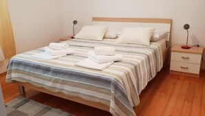 A neatly made bed with striped bedding and white pillows, a bedside table with a lamp, and a small drawer unit. - Apartment Ljiljana (Novi Vinodolski)