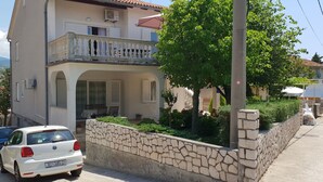 A two-story house with a balcony, parked cars, and a stone wall. - Apartment Ljiljana (Novi Vinodolski)
