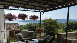 A balcony with a table and chairs, potted plants, and a view of a body of water and mountains. - Apartment Sanja (Brsec)