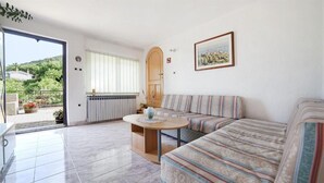 A living room with a sofa, a small table, and a view of a garden through a glass door. - Apartment Sanja (Brsec)