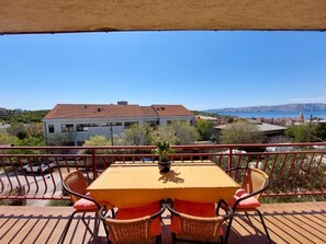 A wooden deck with a table and chairs, overlooking a coastal landscape with buildings and a clear sky.