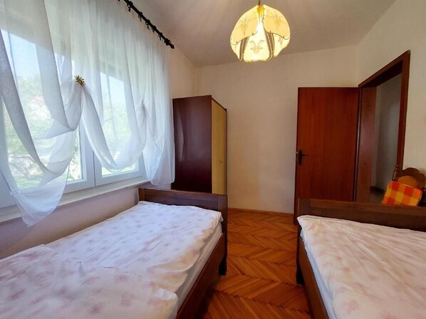 A room with two single beds, a wooden wardrobe, a mirror, and a hanging light fixture.