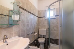 A bathroom with a glass shower enclosure, a white sink, and a toilet. - Apartments Miljenko (Punat)