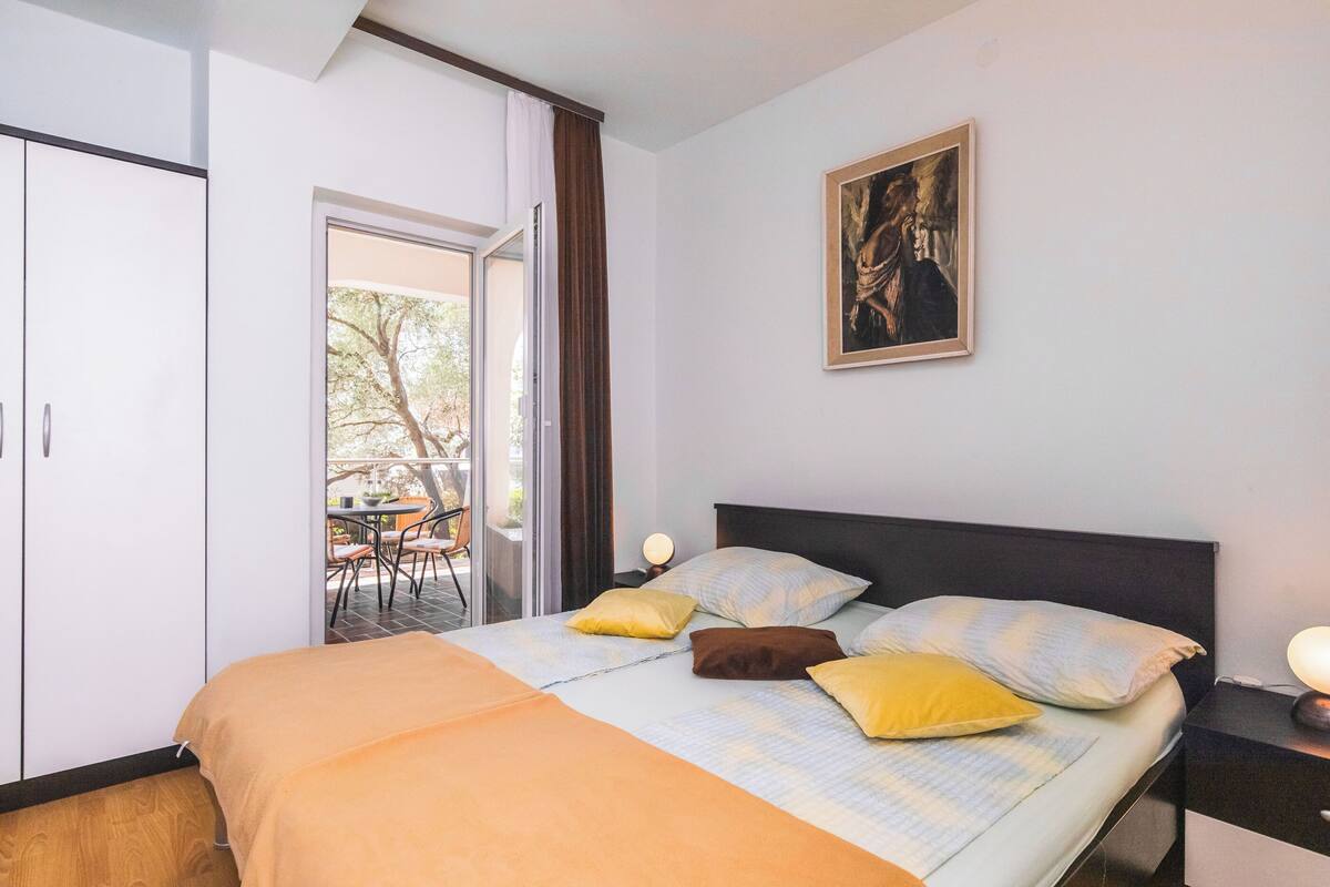 Une chambre à coucher comprenant un lit, une table de chevet, un tableau et donnant sur un espace extérieur.