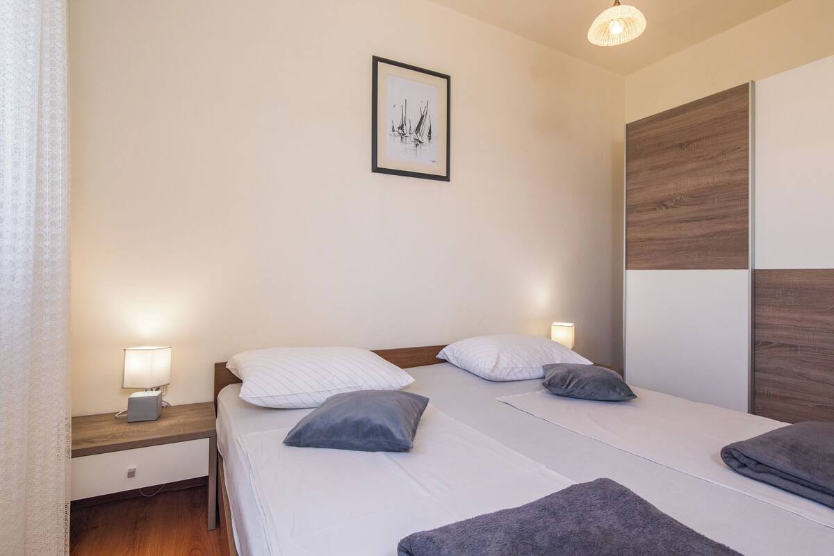 Une chambre d’hôtel avec deux lits, une table de chevet avec une lampe, une œuvre d’art encadrée au mur et un panneau en bois sur le mur.