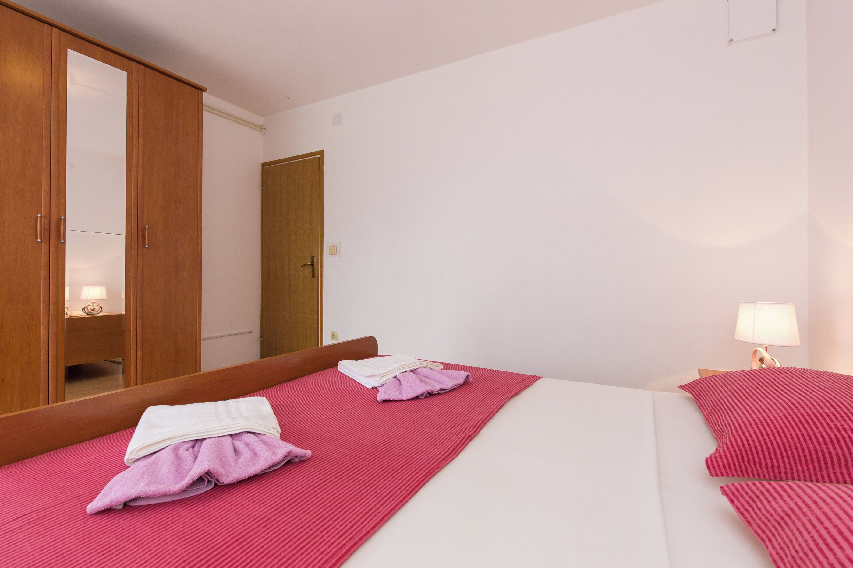 A hotel room with two beds, a large mirror, and a wooden wardrobe.