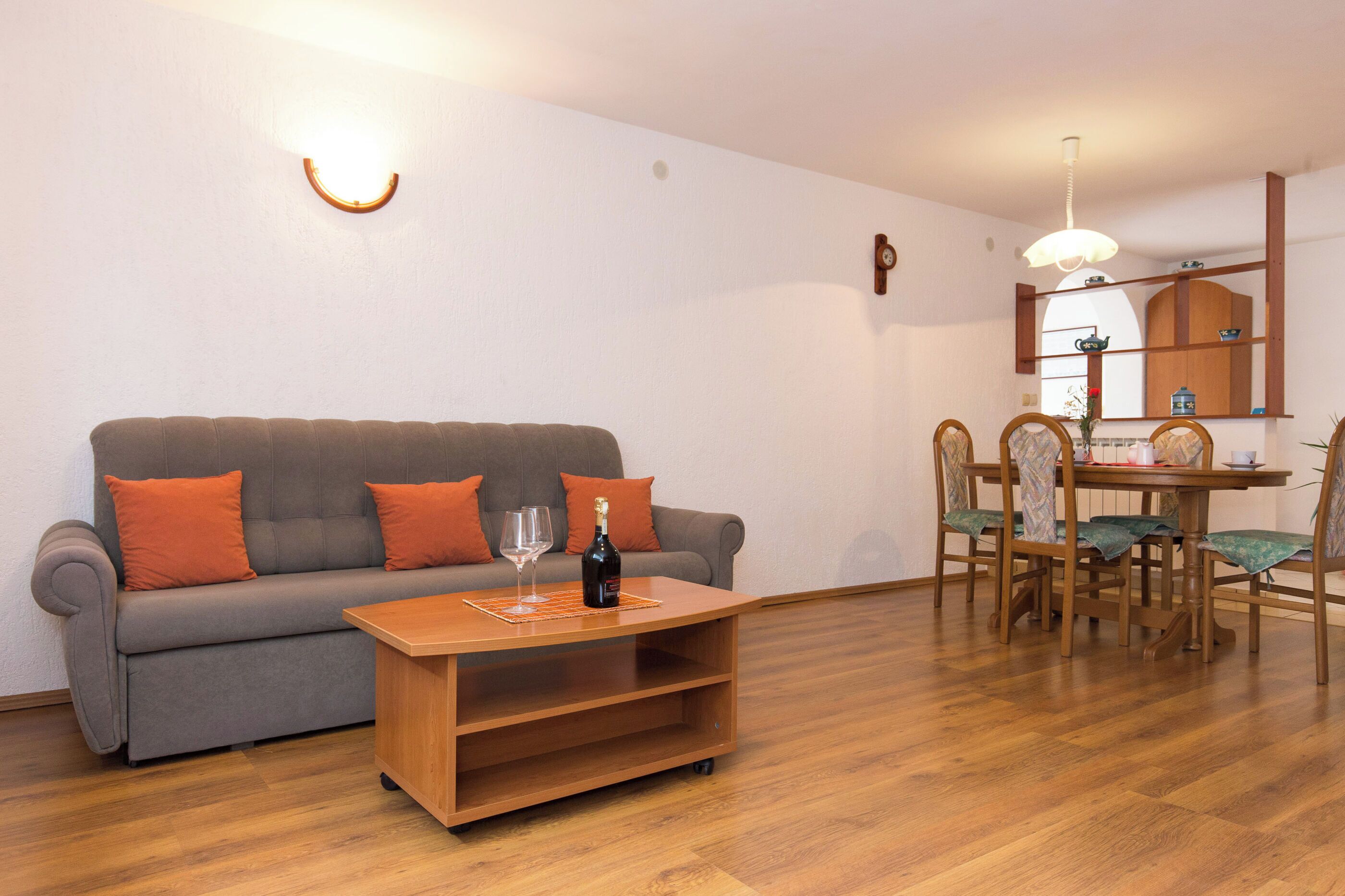 A living room with a grey sofa, wooden coffee table, and a dining area with wooden chairs and a table.