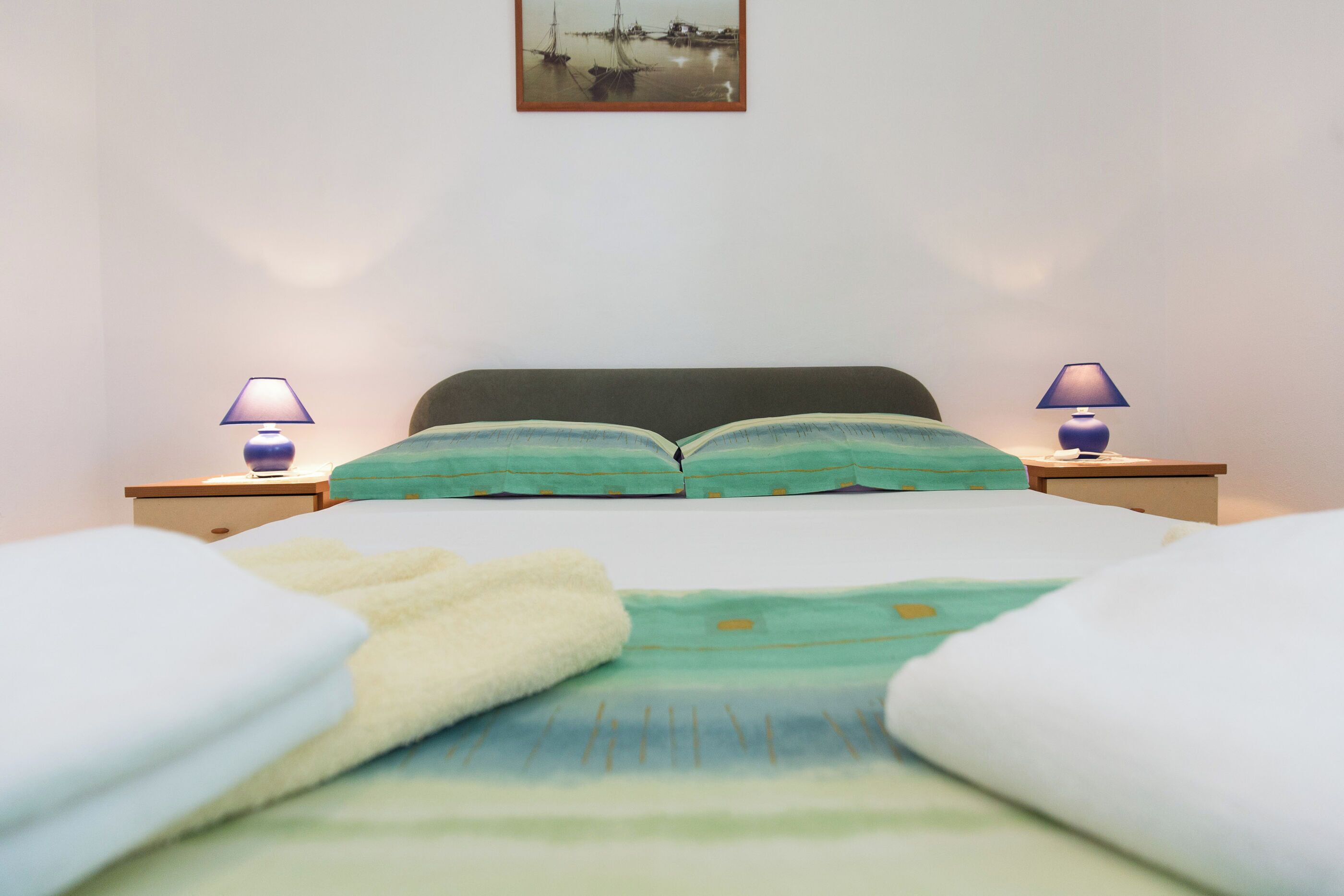A neatly made bed with a green and white striped blanket, two bedside lamps, and a framed picture on the wall.
