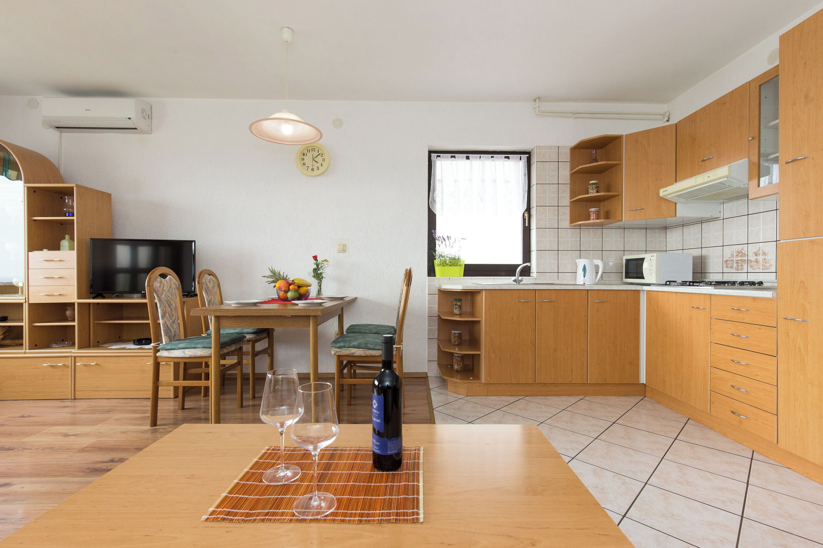 A modern kitchen with wooden cabinets, a dining area with a table and chairs, and a TV in the corner.