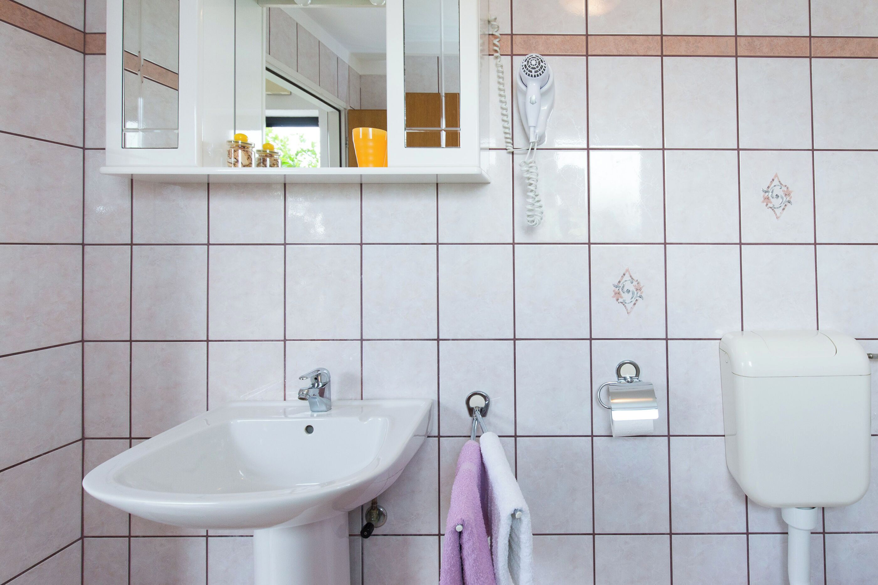 Een badkamer met een witte wastafel, een spiegel, een handdoekhouder en een handdroger.