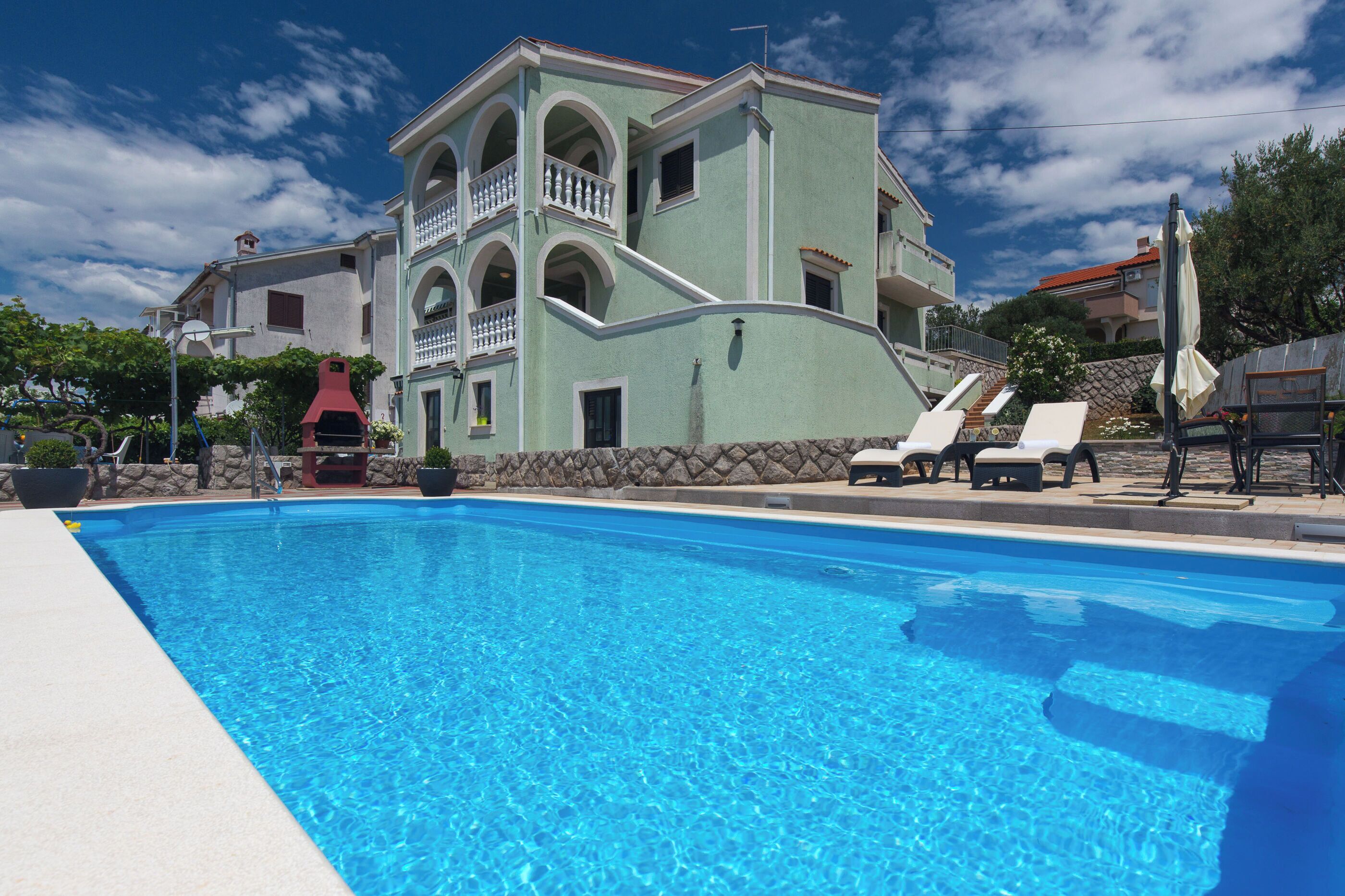 Una piscina con sillas de descanso y un edificio con balcones.