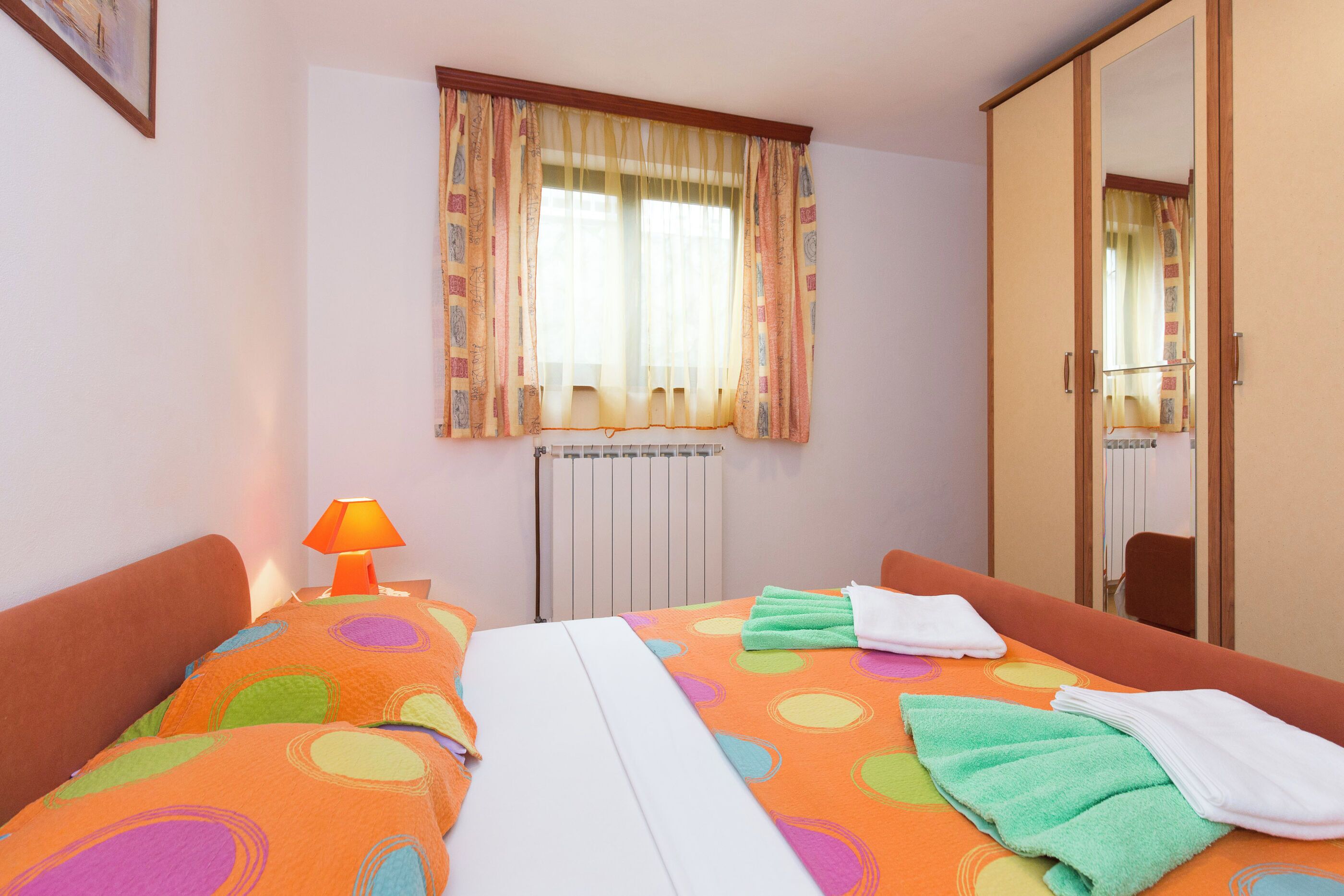 Una habitación de hotel con cama, ventana con cortinas, radiador y espejo.