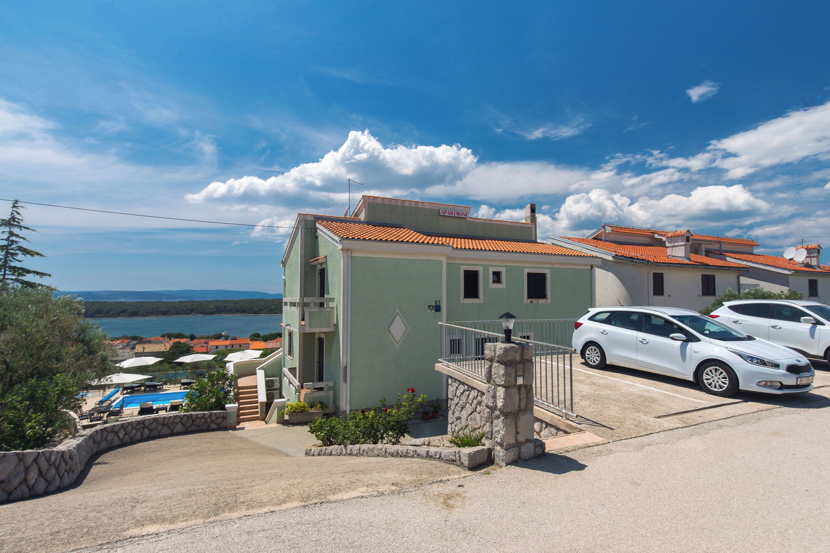 Un edificio de dos plantas con escaleras de piedra y un balcón, piscina y vistas al mar.