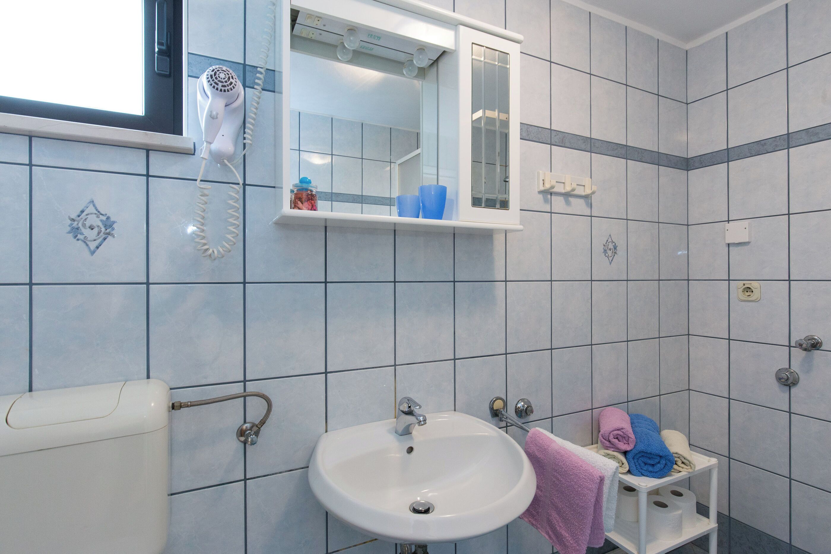 A bathroom with a white sink, a mirror above it, and a hairdryer on the wall.