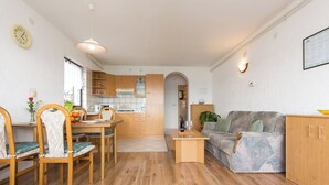 Een moderne woonkamer met een bank, eettafel en stoelen. Er is een keuken met kasten en een raam.