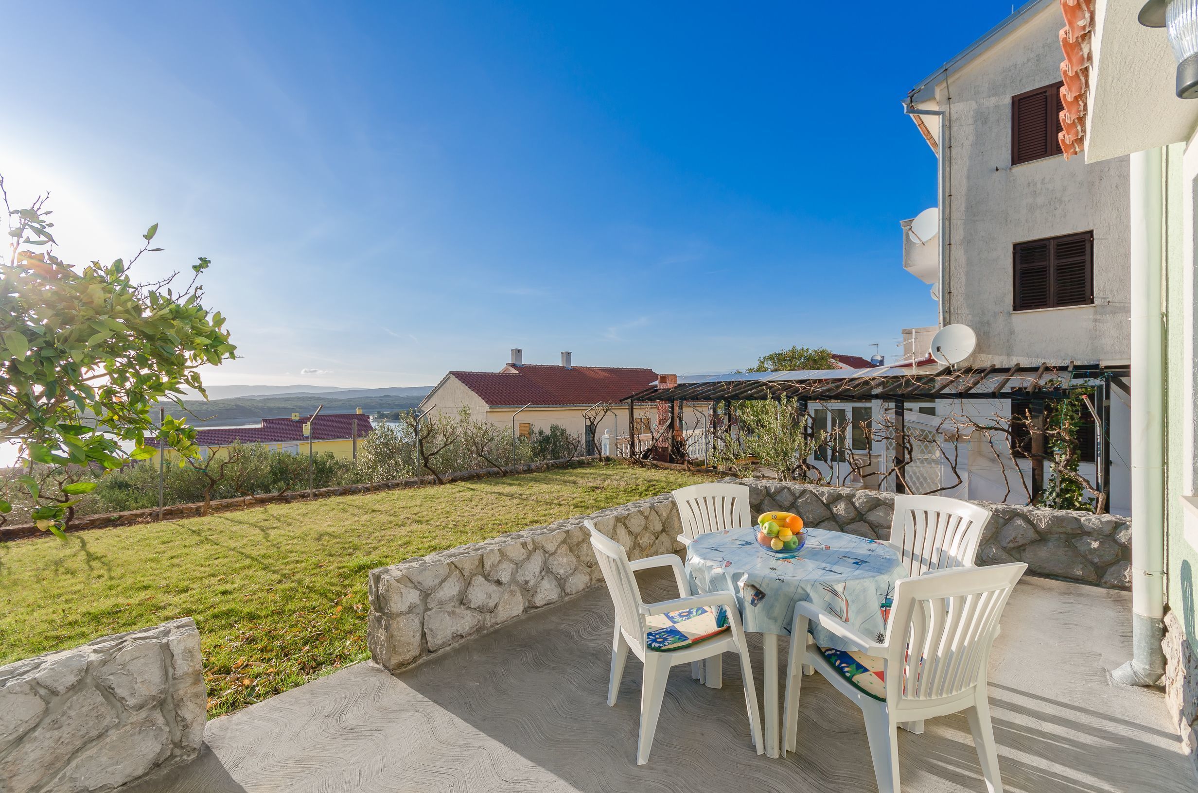 Eine Terrasse mit Tisch und Stühlen, eine Steinmauer und Blick auf ein Haus und die Landschaft.